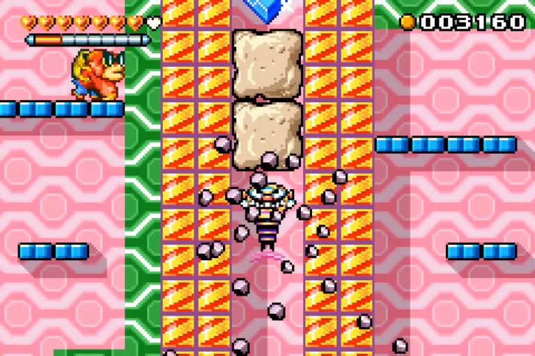 Wario wirbelt als Bohrer durch eine pink‑gelbe Blockschacht, Trümmer fliegen; links oben Herzleiste, rechts Münzzähler, in der Mitte zwei helle Kissenblöcke.