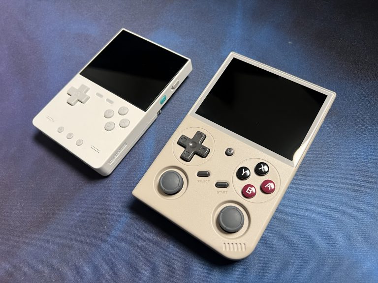 Weißer TrimUI Brick und beiger BATLEXP G350 nebeneinander auf dunklem Hintergrund, beide ausgeschaltet.