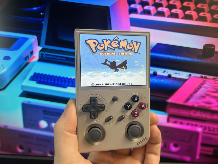 BATLEXP G350 zeigt Pokémon Goldene Edition auf dem Display, gehalten vor bunt erleuchtetem Retro‑Setup mit alten Heimcomputern.
