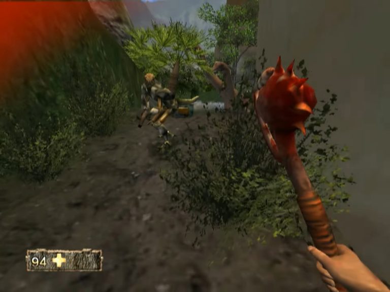 Ego‑Sicht in einem schmalen Felspfad, Spieler hält eine schwere Keule mit roten Stacheln, Gegner stürzt nach Treffer, Blutspuren und dichter Bewuchs im Hintergrund.