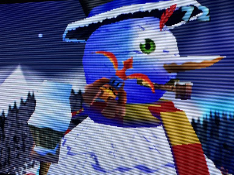Foto eines TV Bildschirms mit sichtbaren Scanlines, Nahaufnahme eines Schneemanns mit grünem Auge und rotem Schal in einem N64 Spiel. Winterliche Szene mit dunklem Himmel, die Texturen und Kanten sind klar erkennbar.